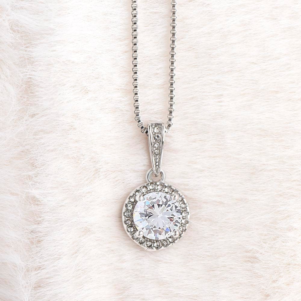 A necklace with a gold finish and a big cubic zirconia crystal pendant laying on a white furry carpet.