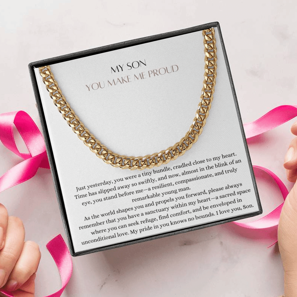 A person unwrapping a necklace gift, with a big Cuban chain necklace with a yellow gold finish, and a message card that says to my son.