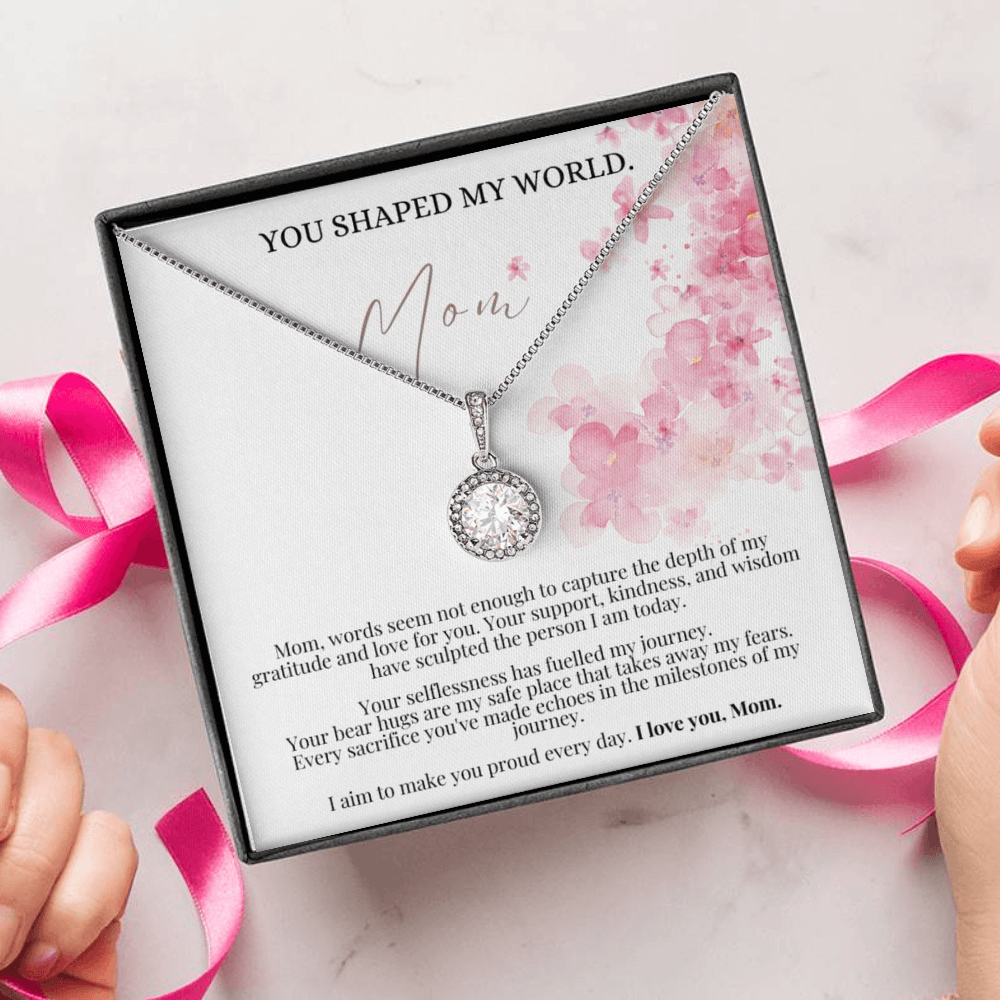 A person unwrapping a necklace gift, with a big cubic zirconia crystal pendant and a white gold finish, with a message card to mom.
