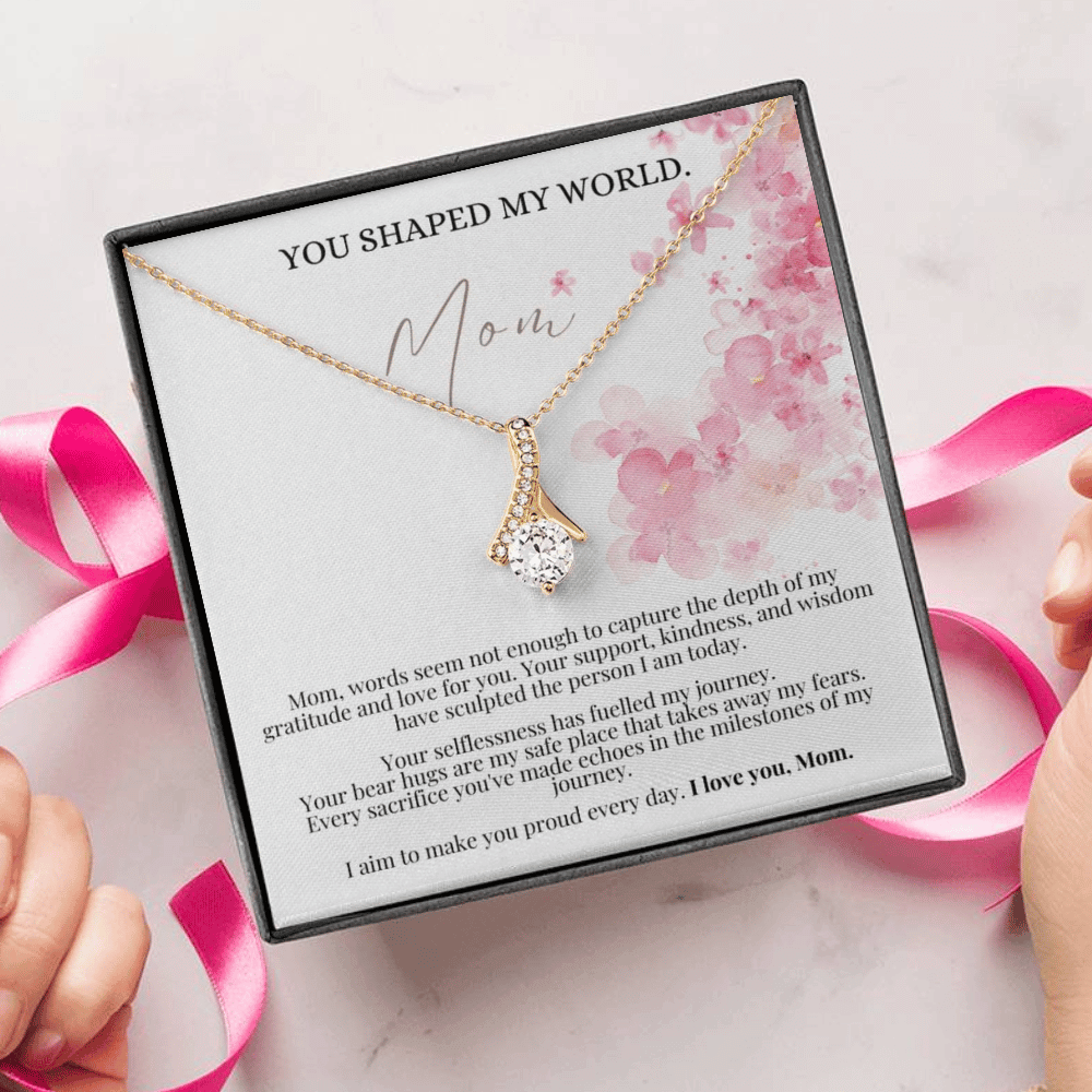 A person unwrapping a necklace gift with ribbon shaped pendant with cubic zirconia crystals and white gold finish, with a mother's day message card.