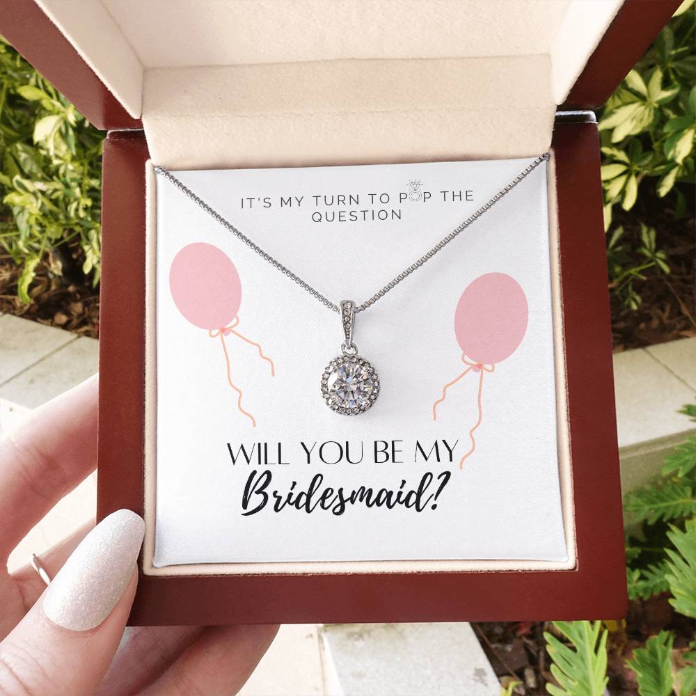 A woman holding a mahogany Jewelry box with a big cubic zirconia crystal pendant and a white gold finish, with a message card to bridesmaids.