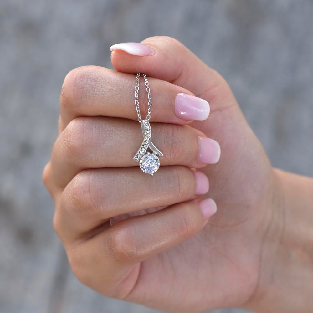 A woman touching a necklace on her neck with ribbon shaped pendant with cubic zirconia crystals and a gold finish.