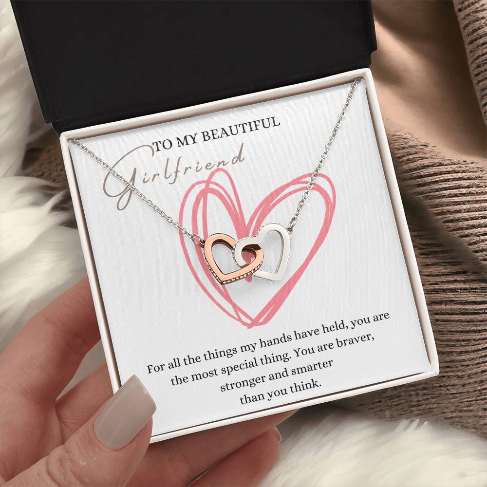 A woman holding a jewelry box, with a necklace with two connected hearts embellished in cubic zirconia crystals and white gold finish, with a message card to my beautiful girlfriend.
